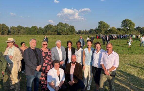 Sir David Attenborough and other guests in a group on a grassy floodplain of the Thames at Syon Park.