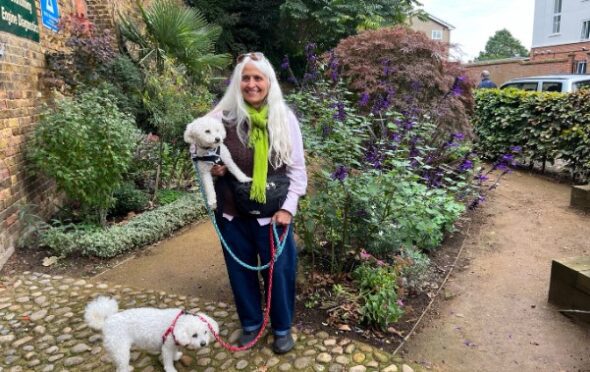Image of Bharti Hindocha smiling and standing in the gardens holding one white poodle under her arm with another on a lead by her feet.