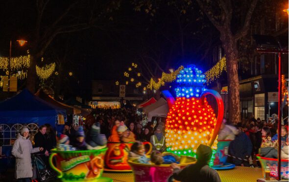 Image from Kew Sparkle showing a brightly lit child's merry go round in the foreground and a street filled with people looking at market stall behind