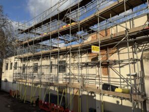 Exterior view of Caxton House by Kew Bridge, wreathed in scaffolding with bare brickwork exposed where Banksy's Goat has been removed.